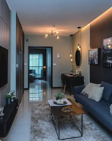 A stylish 3 bedroom apartment interior featuring a cozy living room with a navy sofa, a coffee table, decorative lighting, and a glimpse into a bedroom through an open door.