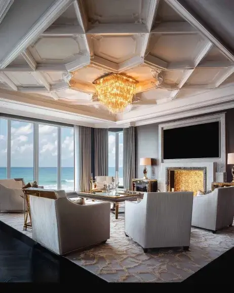 Luxurious living room with a geometric tray ceiling design, a grand crystal chandelier, and ocean-view windows.